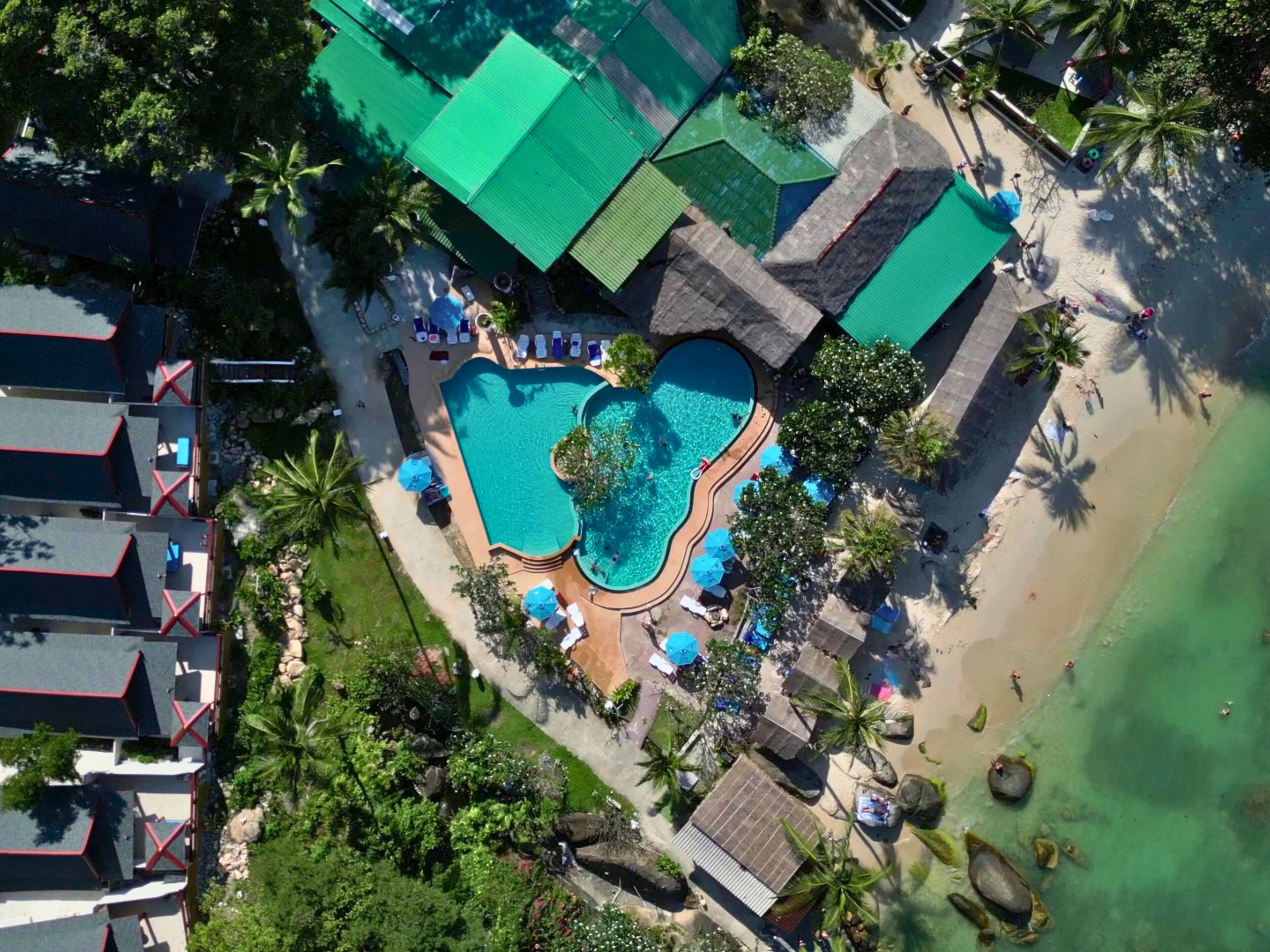 Vista aérea de un resort con piscina central, varias cabañas tipo bungalow y una zona de playa.