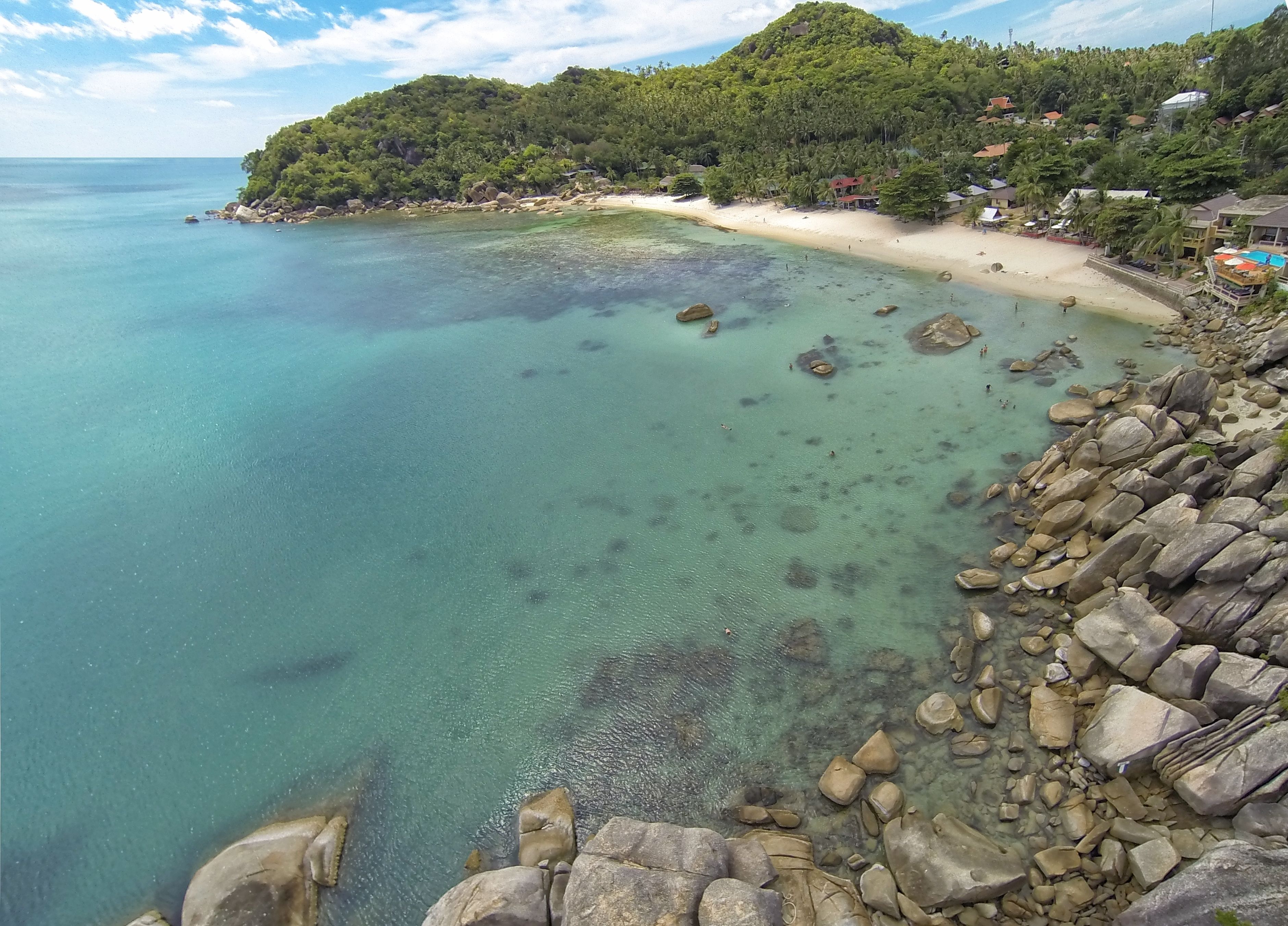 Vista costera con aguas turquesas cristalinas, una playa de arena y un litoral rocoso.