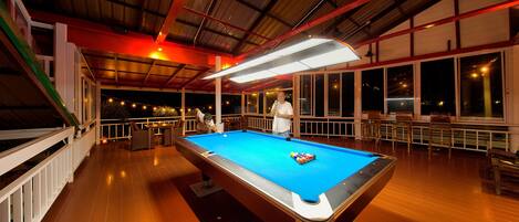 A pool table in a spacious indoor area with a high ceiling and large windows.