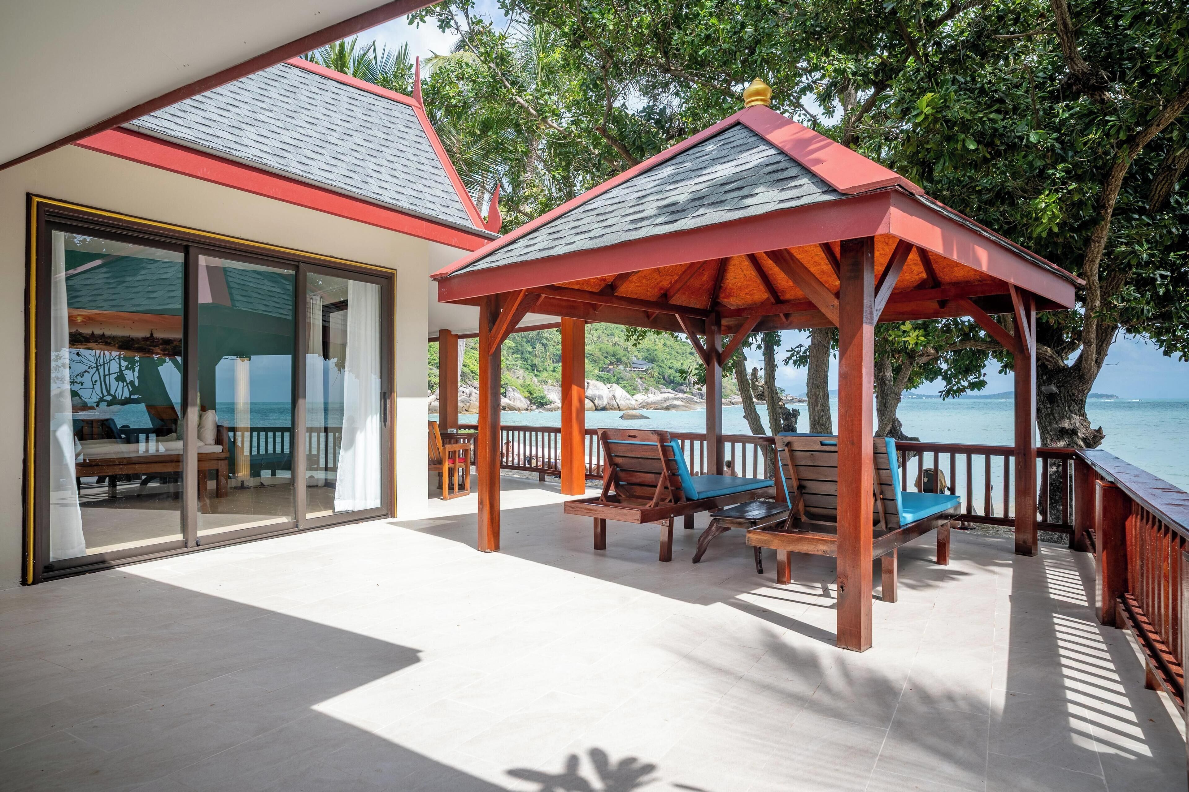A covered outdoor area with wooden furniture and a glass door leading to a pool area.
