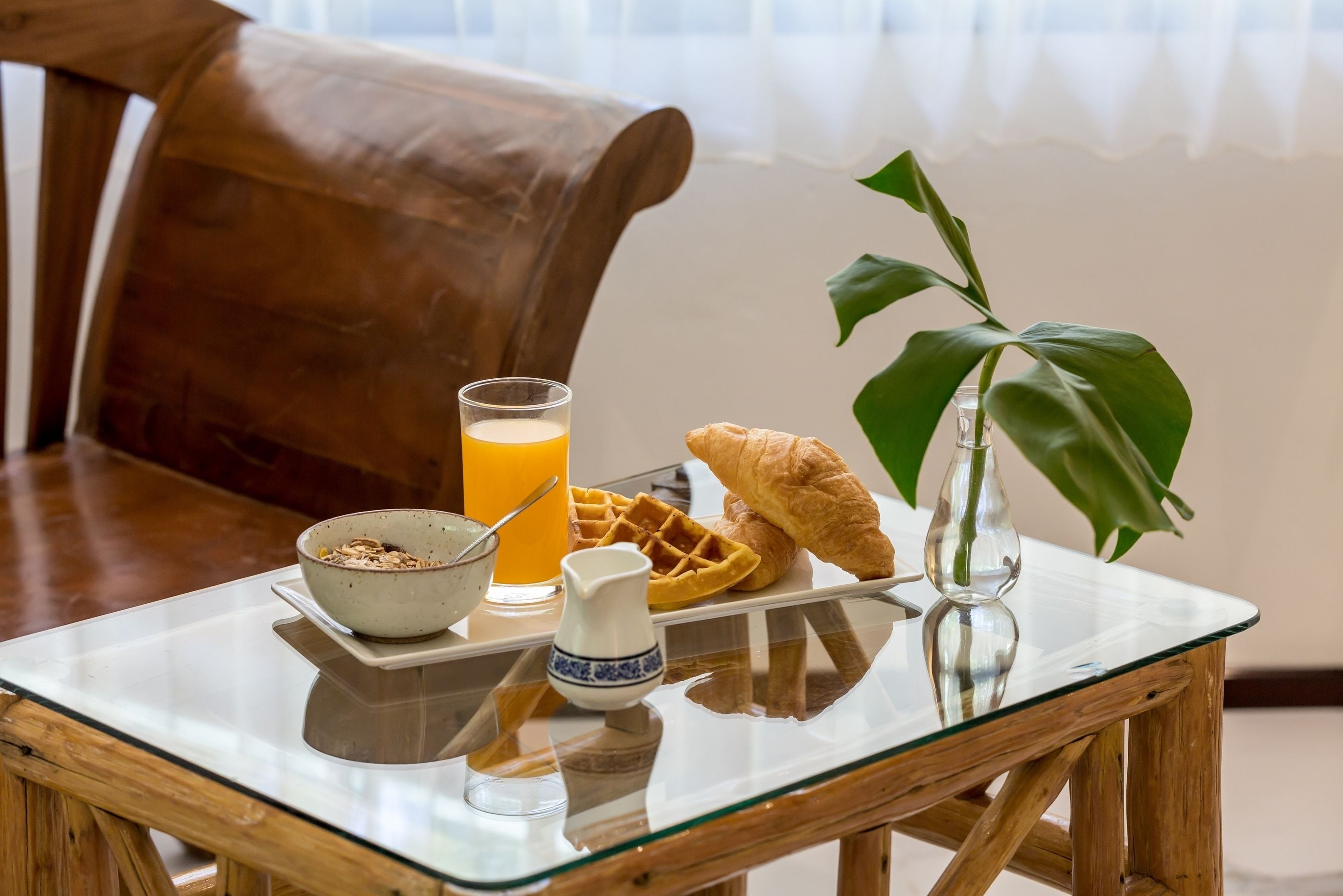 Une table de petit-déjeuner avec un bol de céréales, un verre de jus d’orange, un gaufre, un croissant et un petit pichet.