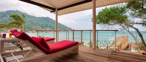 Una terraza de madera con una silla lounge roja y una mesa de vidrio con un jarrón de flores.