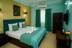 A hotel room with a bed, a nightstand, a desk with a vase of flowers, a wardrobe, and an air conditioning unit. - Hotel Eurostar International (New Delhi)