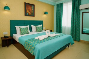 A hotel room with a bed, two bedside tables, a nightstand, a painting on the wall, a window with curtains, and an air conditioning unit. - Hotel Eurostar International (New Delhi)