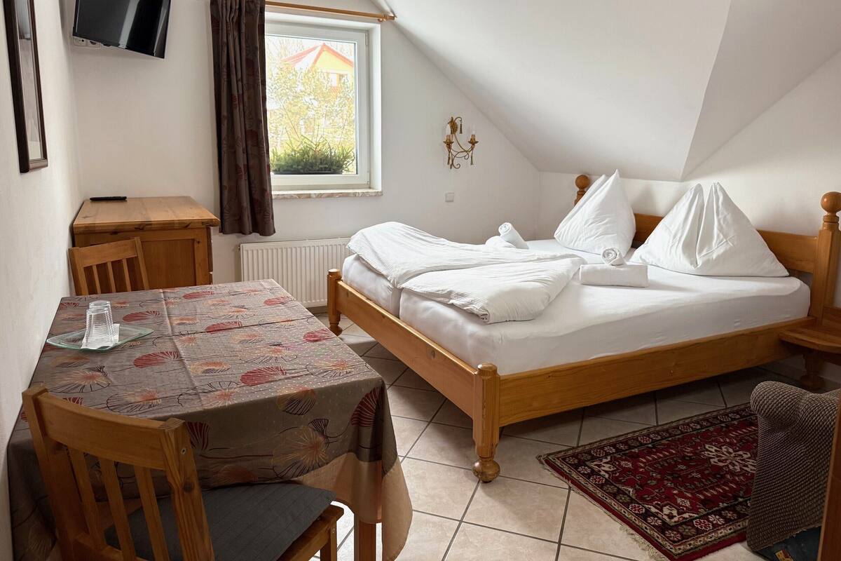Une chambre à coucher avec un lit, une table, une chaise, un téléviseur et une fenêtre.