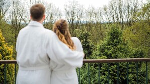 A couple standing on a balcony overlooking a forested area. - Seeberg (Poustka)