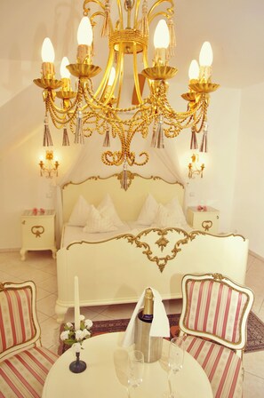 Un dormitorio lujoso con cama blanca, candelabro dorado ornamentado y decoración a juego.