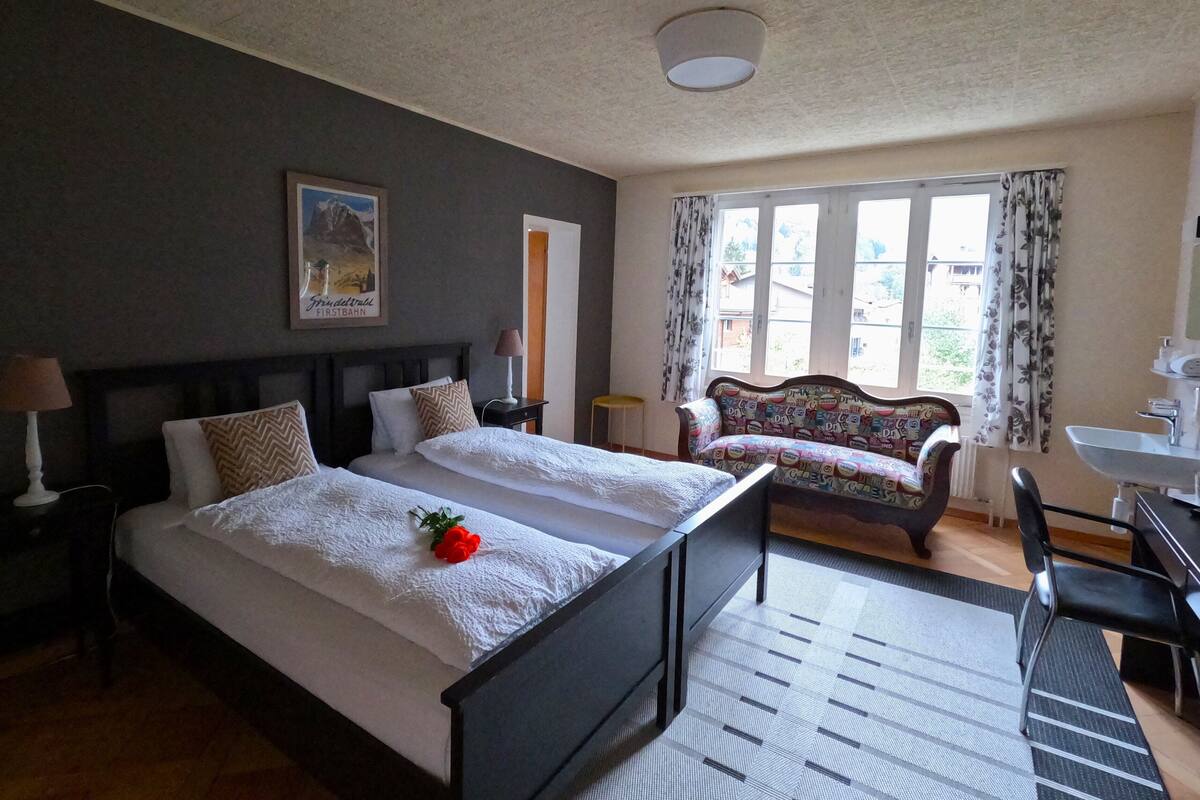 Une chambre d’hôtel avec un grand lit, un canapé, un bureau avec une chaise et une fenêtre avec des rideaux.