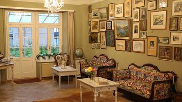 A room with a large window, a chandelier, a sofa with a colorful pattern, and a wall adorned with framed pictures.