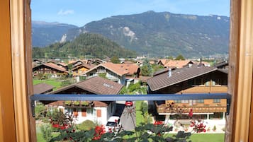 A view of a mountain village with traditional wooden houses, a clear sky, and a road with a red car.