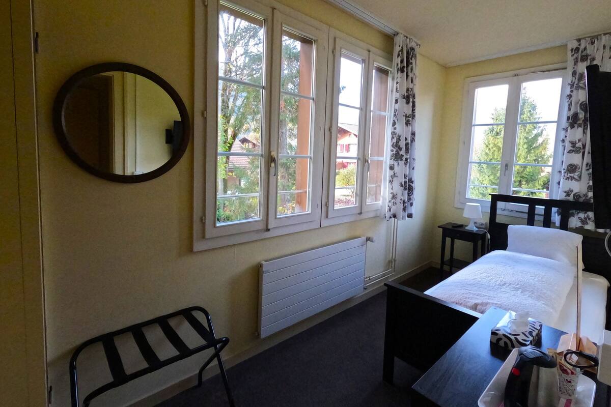 Une chambre à coucher avec un lit, une table de chevet, une chaise, un radiateur et une fenêtre avec des rideaux.