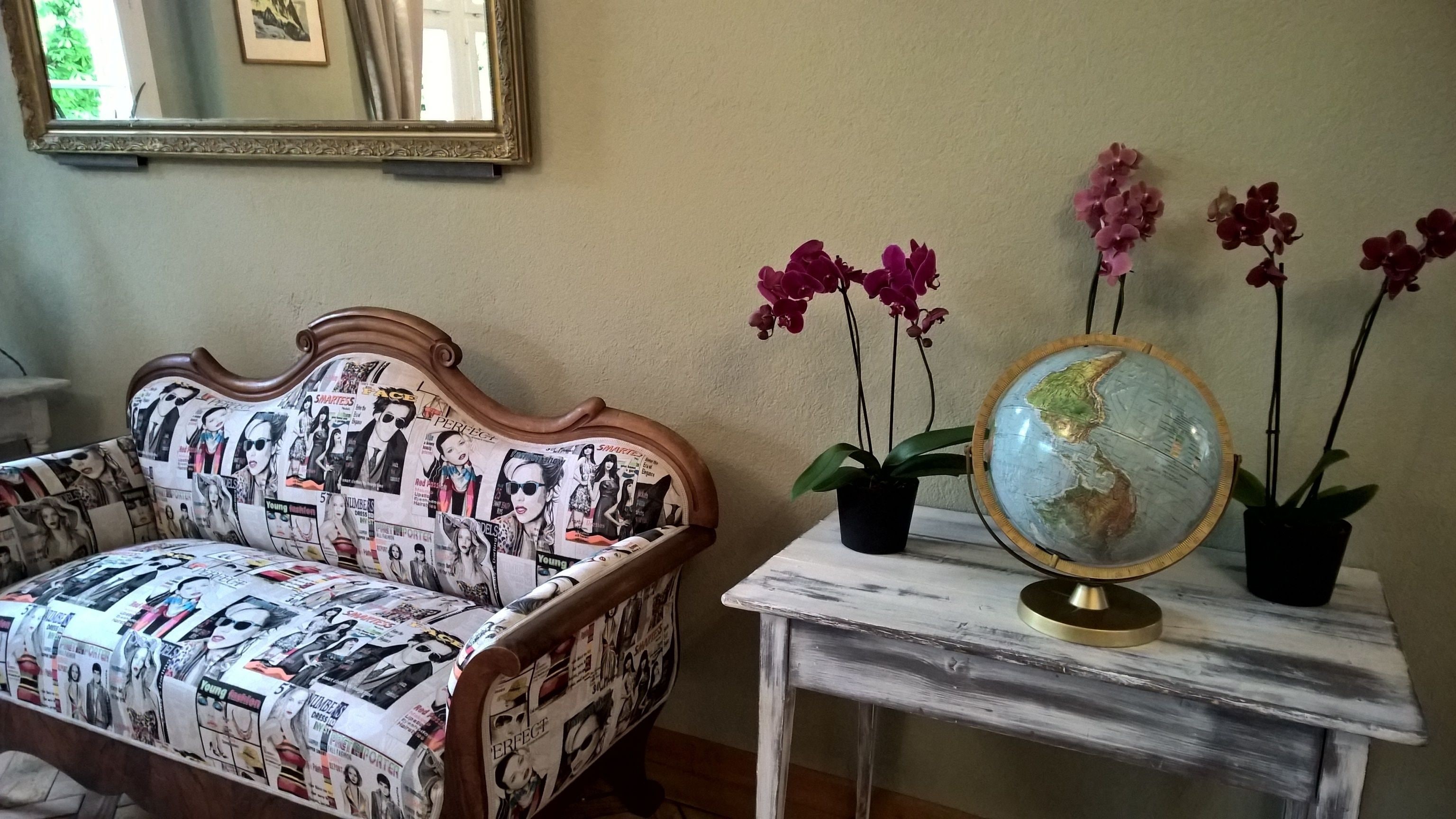 Una habitación con un sofá estampado, un globo terráqueo sobre una mesita y dos orquídeas en macetas.