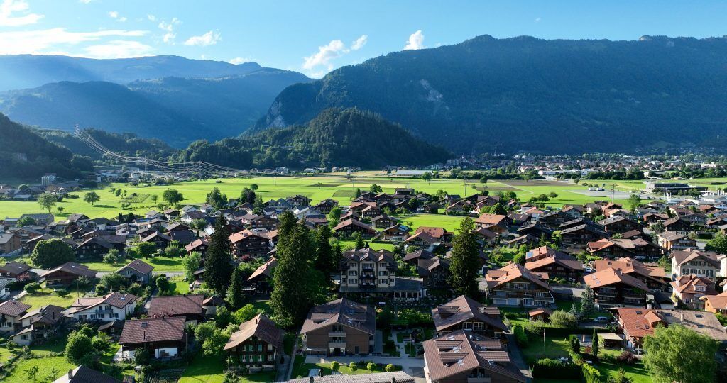 A residential area with houses, a large building, and mountains in the background.