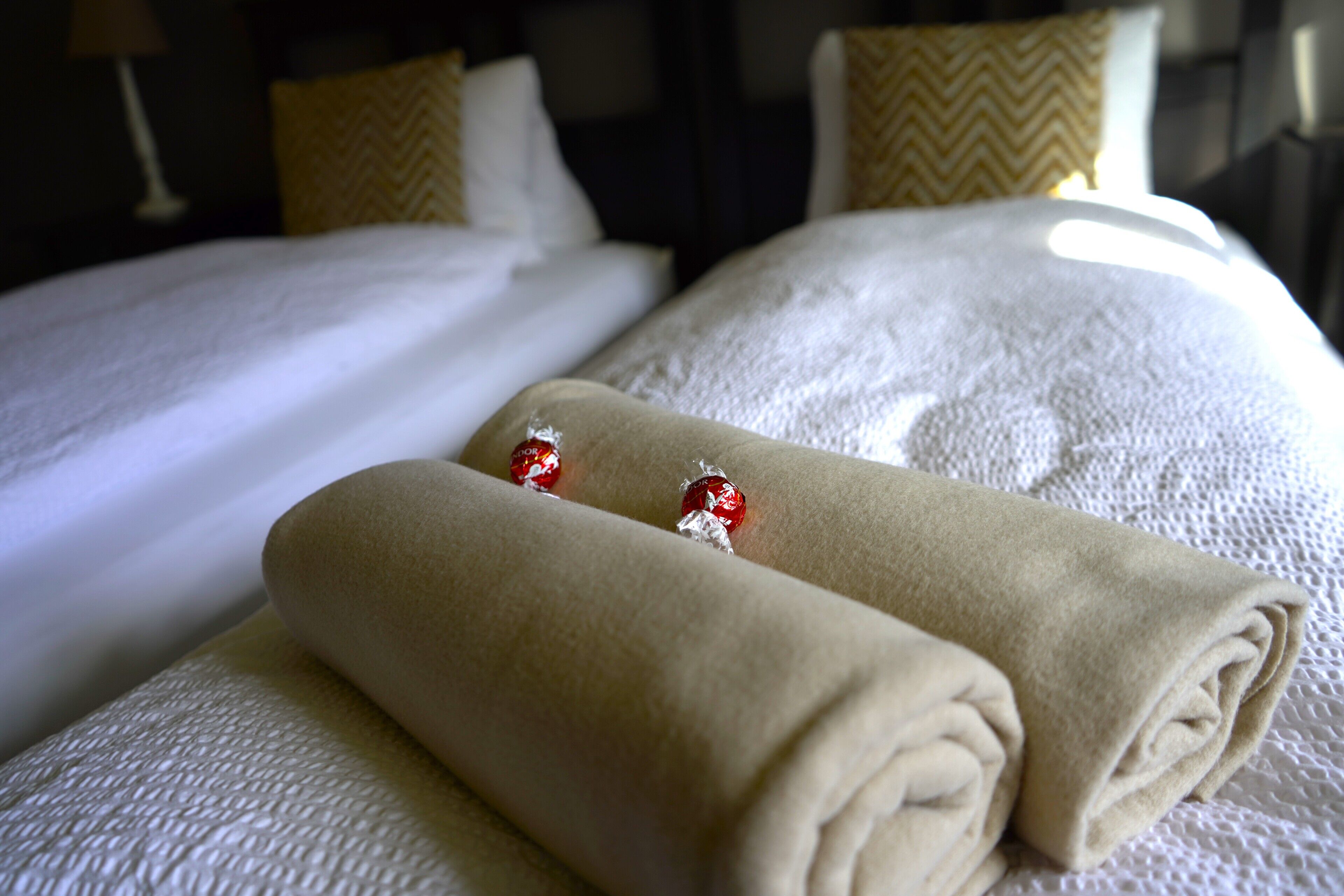 A neatly made bed with two rolled towels and two red decorative items on the pillows.