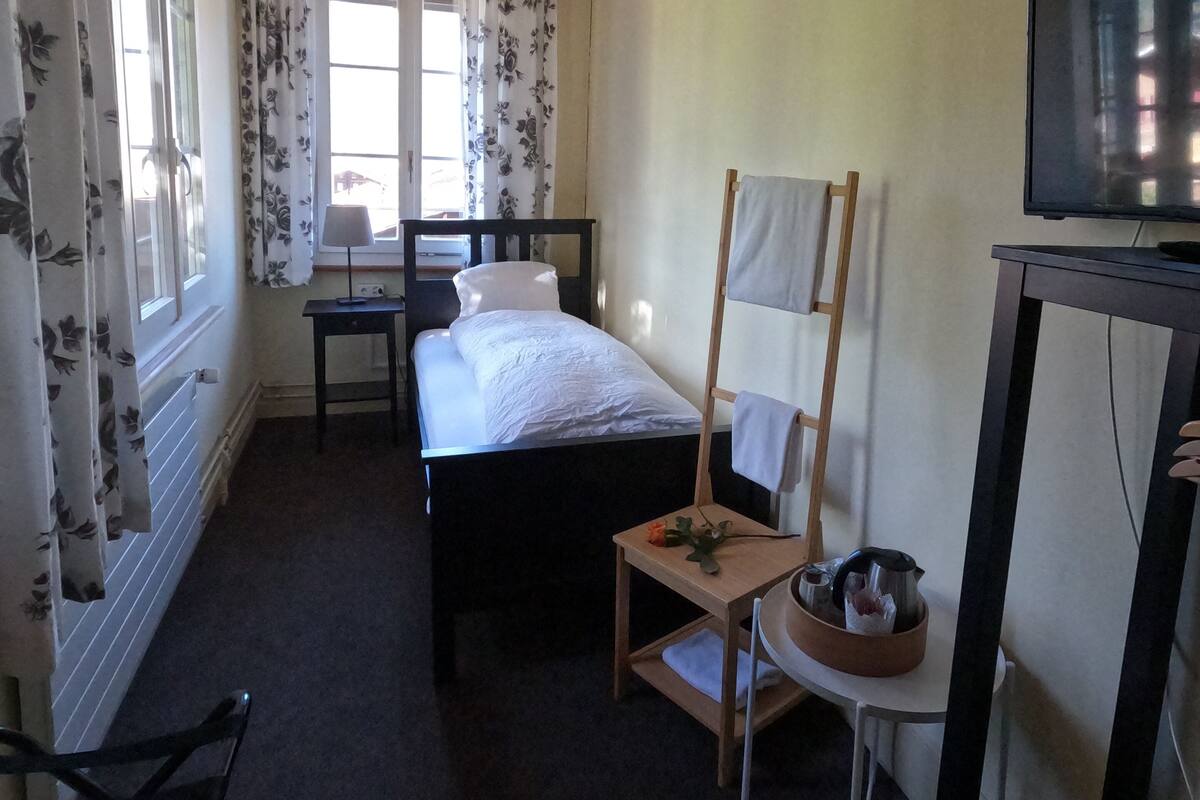 Une chambre à coucher comprenant un lit, un bureau, une chaise, un téléviseur et une fenêtre avec des rideaux.