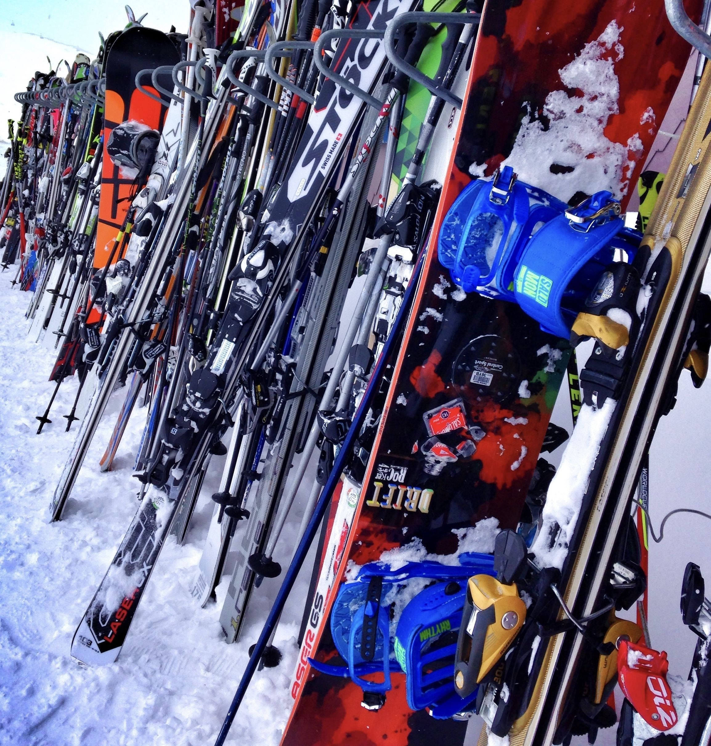 A row of skis leaning against a wall, with snow on the ground.