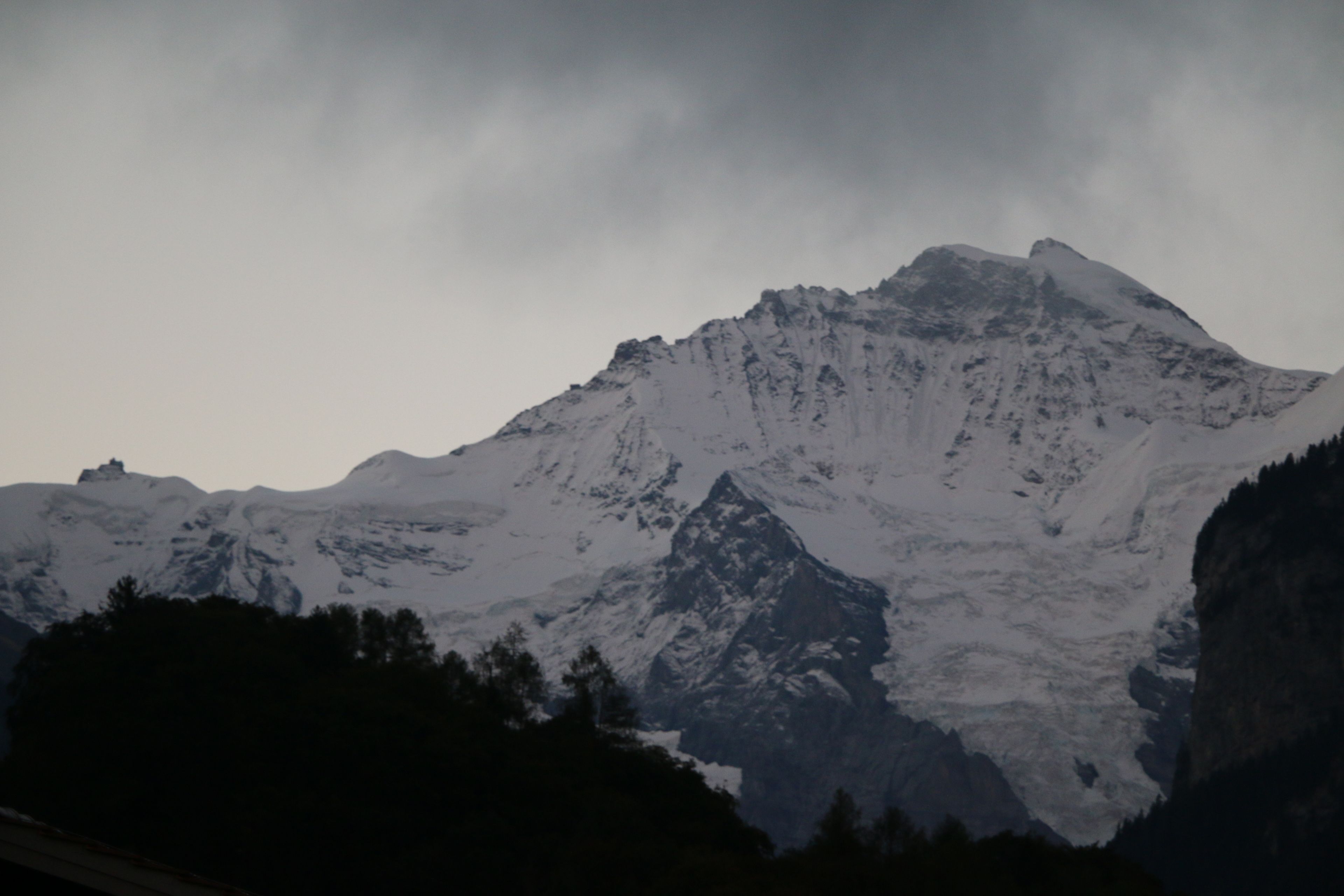 A mountain with snow-covered peaks and a forested foreground.