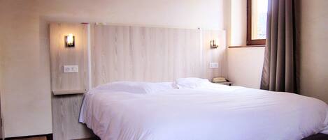 Ein Schlafzimmer mit einem großen Bett, Nachttischlampen, einer Holzbank und einem Fenster mit Vorhängen.