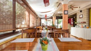 A restaurant with wooden tables and chairs, a central floral arrangement, and a ceiling fan. - Villa Cezar (Kastela)