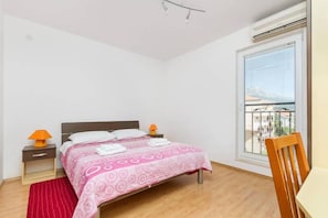 Quarto com cama, mesas de cabeceira, uma cadeira e janela com vista.