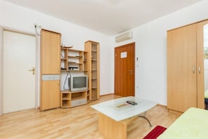 Quarto compacto com guarda-roupa de madeira, uma pequena TV em uma prateleira, uma mesa com um controle remoto e uma porta com uma placa.