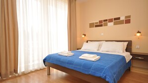 A hotel room with a bed, curtains, a wall with a light switch, and a wooden floor. - Villa Cezar (Kastela)