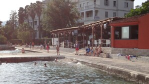 A public swimming area with a pool, a covered seating area, and a building in the background. - Villa Cezar (Kastela)