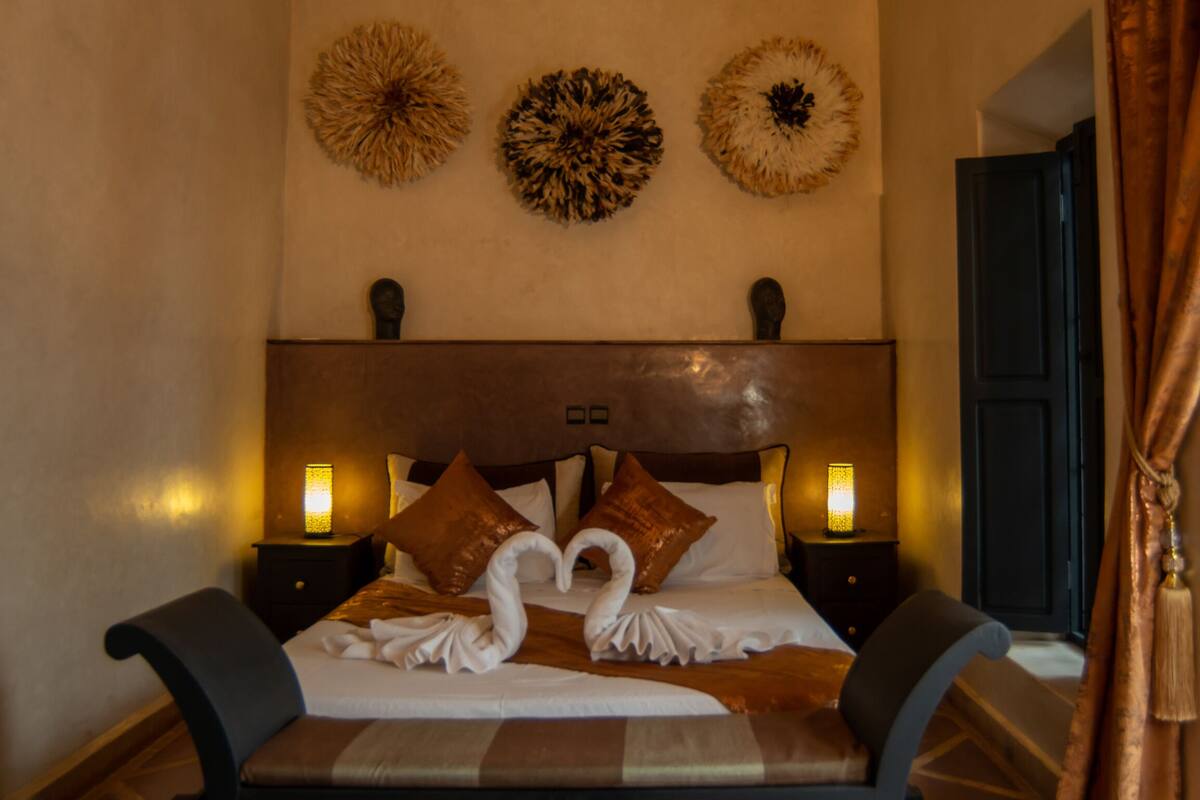 A hotel room with a large bed, two nightstands, decorative wall art, and a door.