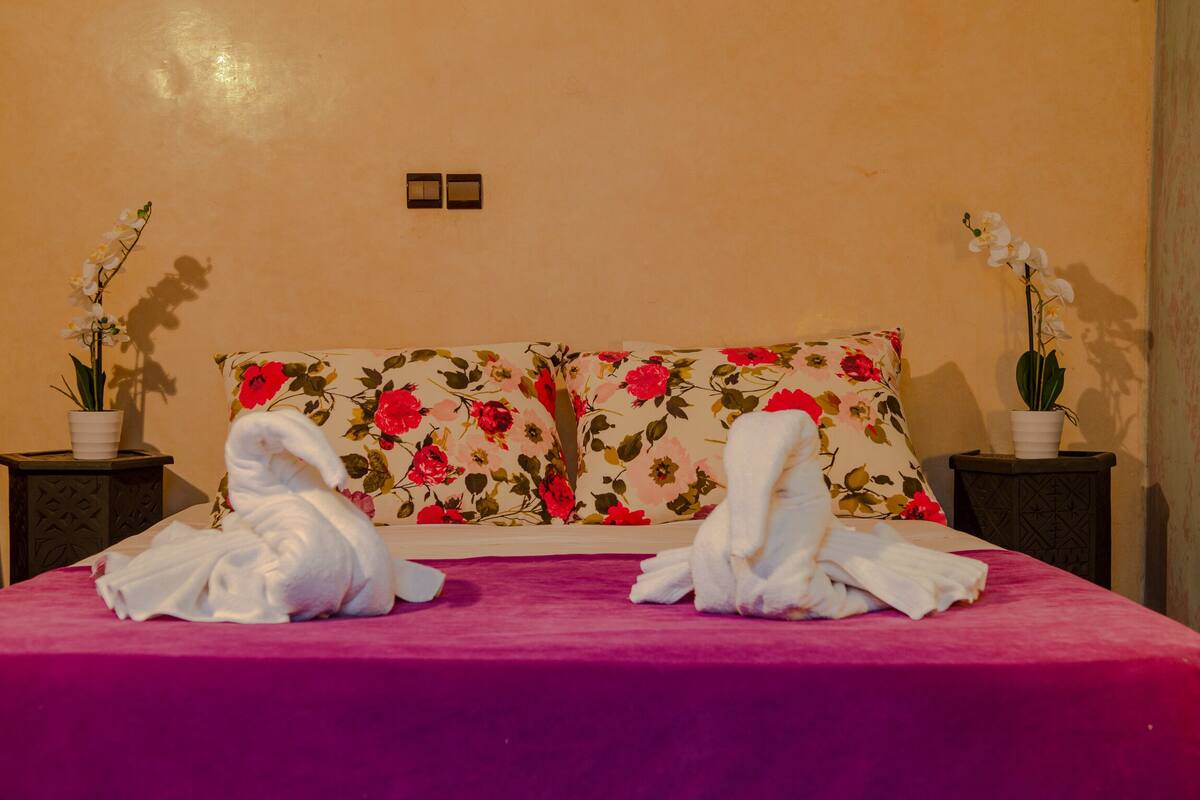 A neatly made bed with floral pillows and two towels.