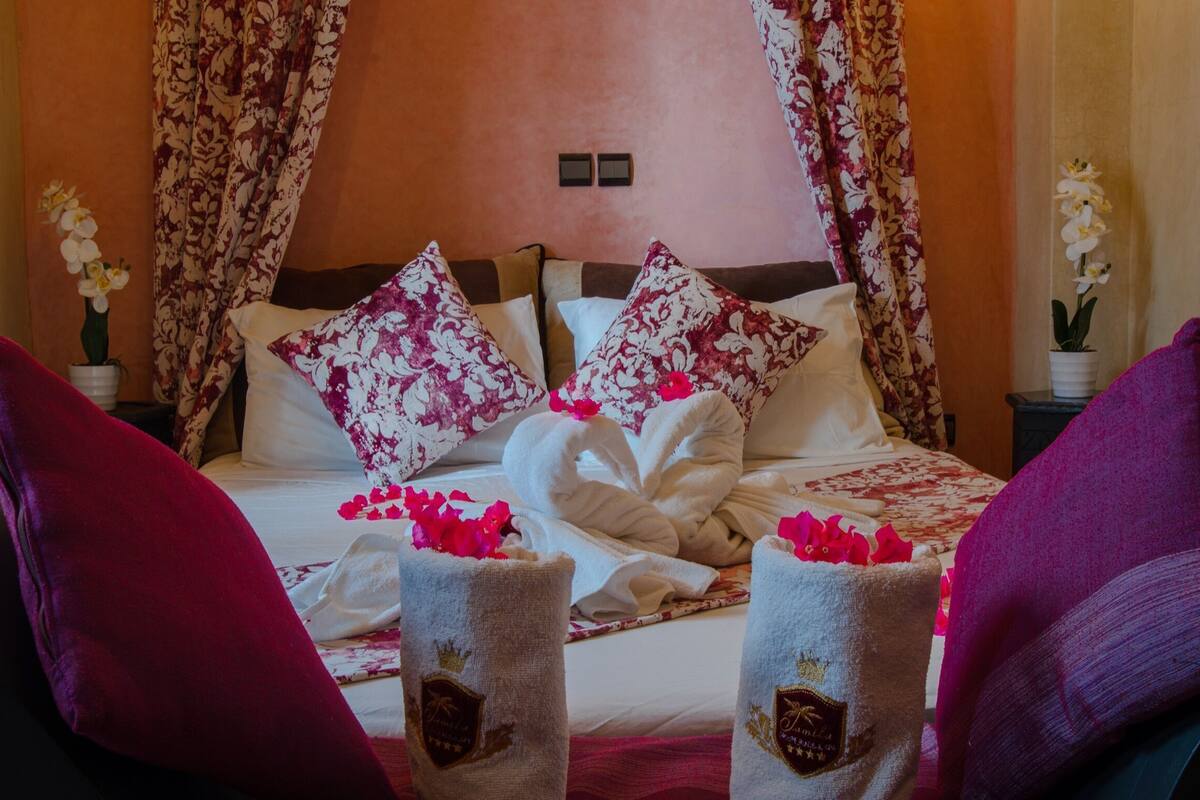 A hotel room with a bed, floral curtains, and two towels with a crest emblem.