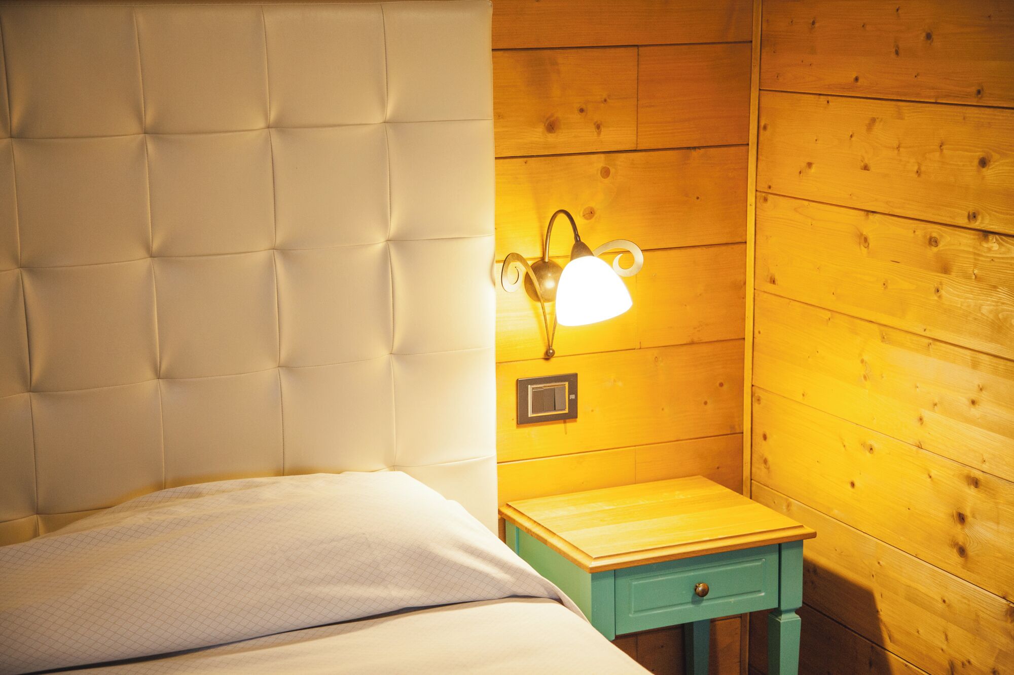 Een slaapkamer met een gestoffeerd hoofdeinde, een nachtkastje met een lamp en een houten wand.