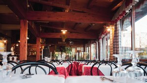 Een restaurant met houten balken, tafels met rode tafelkleden en hangende lampen.