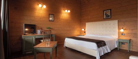 A wooden-paneled room with a bed, a desk, and a chair. There are wall-mounted lights and a picture on the wall.