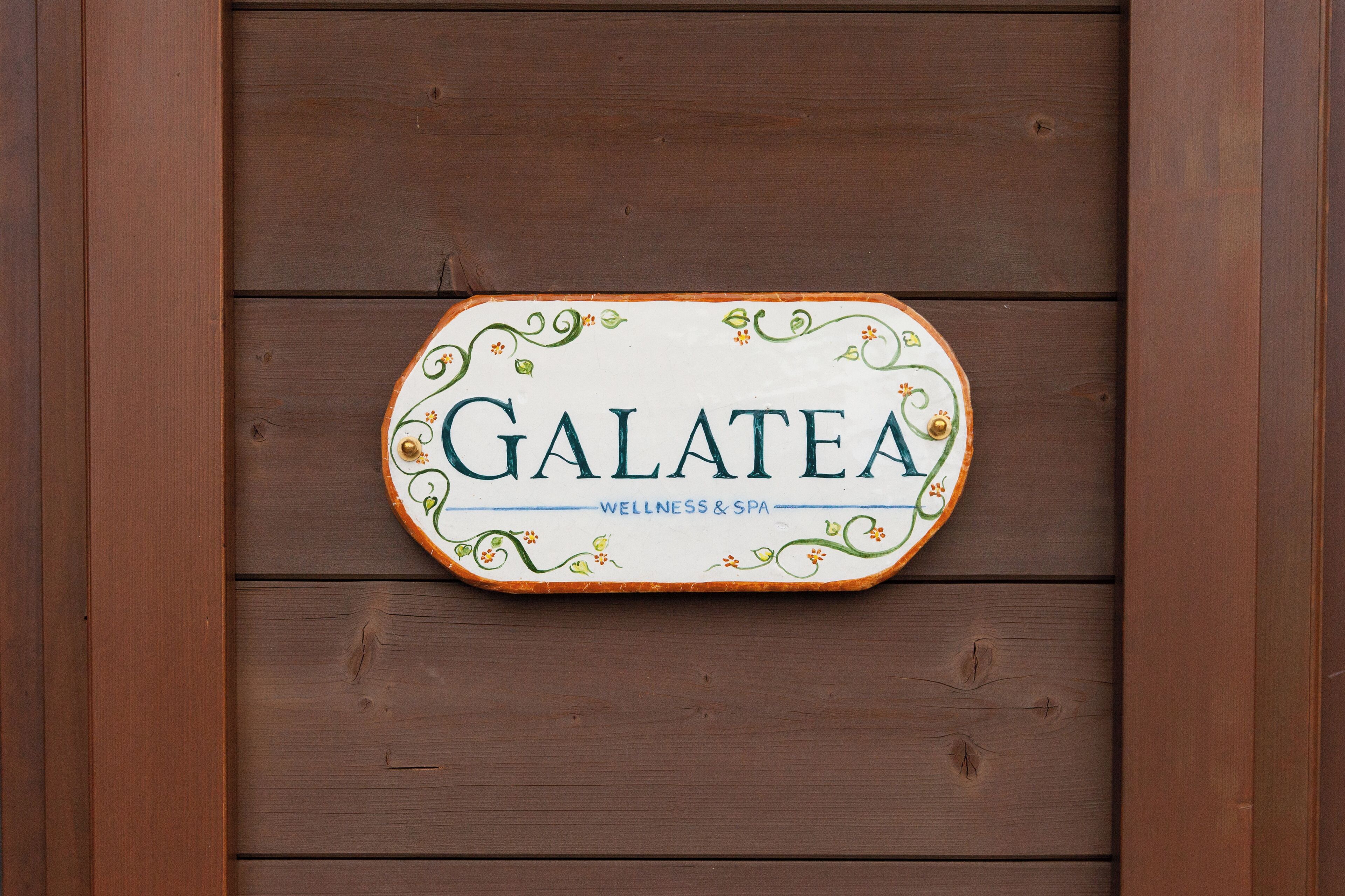 A sign with the name "GALATEA" and the words "WELLNESS & SPA" on a wooden wall.