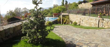 A stone pathway leading to a pool area with a stone wall and metal fence.
