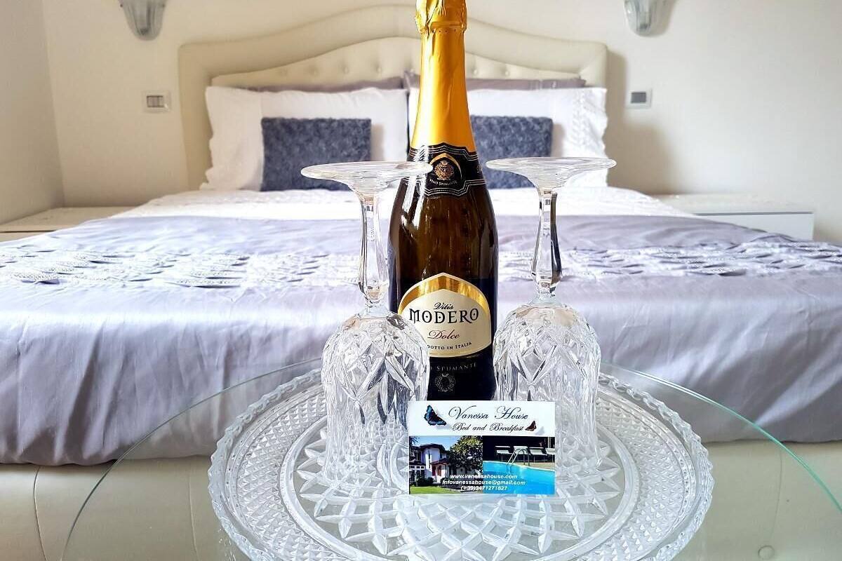 A bed with a white headboard, a bottle of wine, and two wine glasses on a clear glass tray.