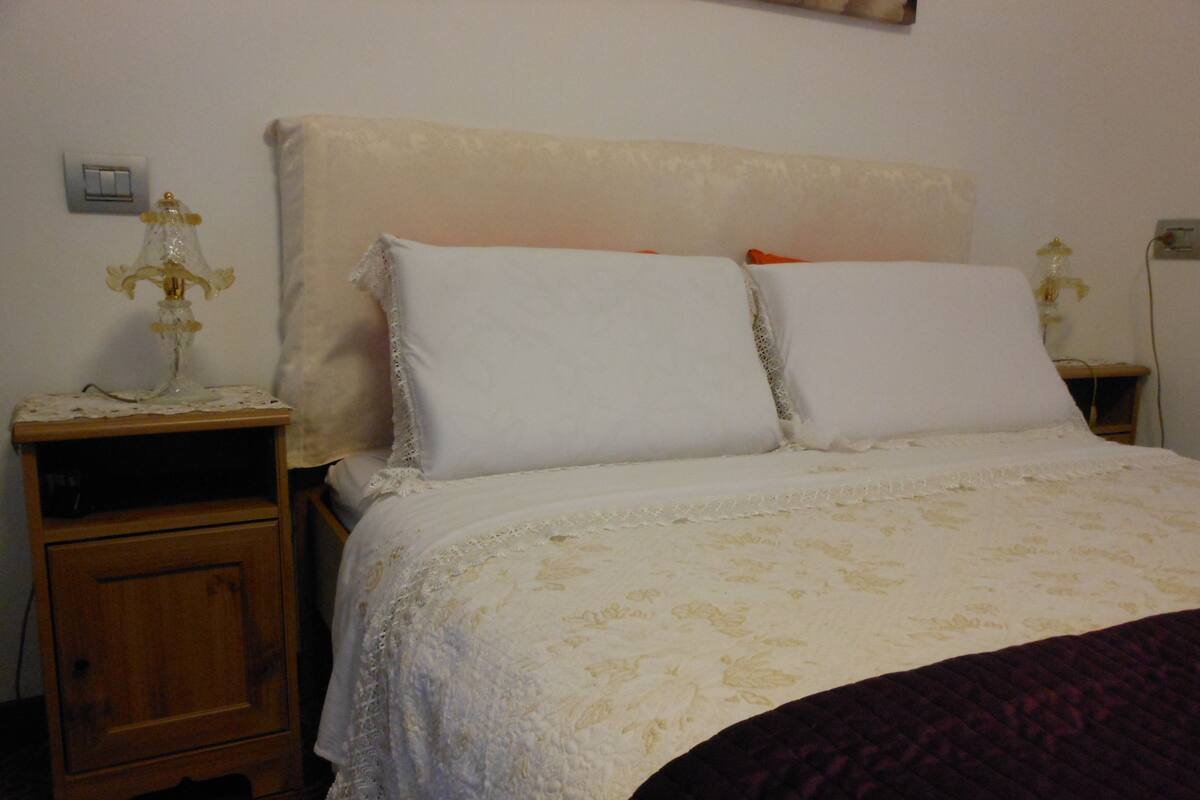 A bedroom with a bed, two nightstands, and a wall-mounted light switch.