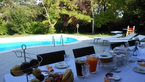 Área de refeições ao ar livre com piscina ao fundo, cercada por vegetação exuberante.