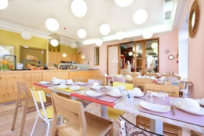 A restaurant with multiple tables set for dining, wooden chairs, and hanging pendant lights. - Hotel Hermès (Marseille)