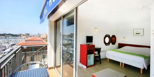 Habitación de hotel con balcón, cama, televisor y escritorio pequeño.