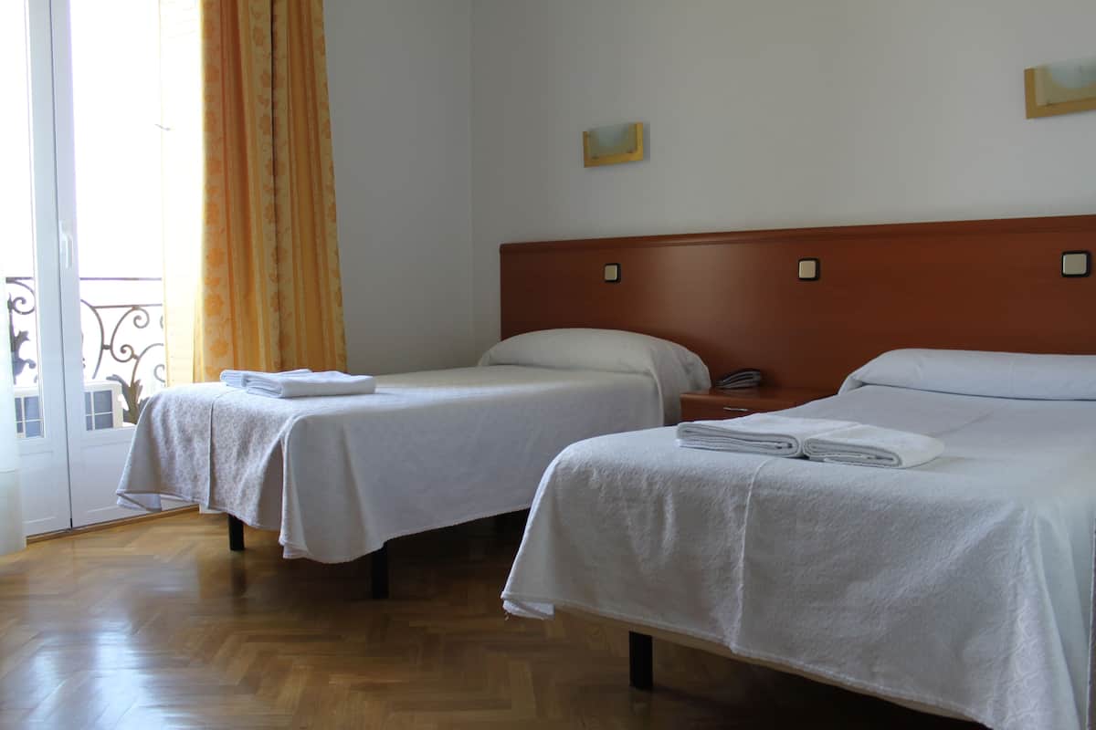 A hotel room with two single beds, wooden headboards, and a wooden floor.