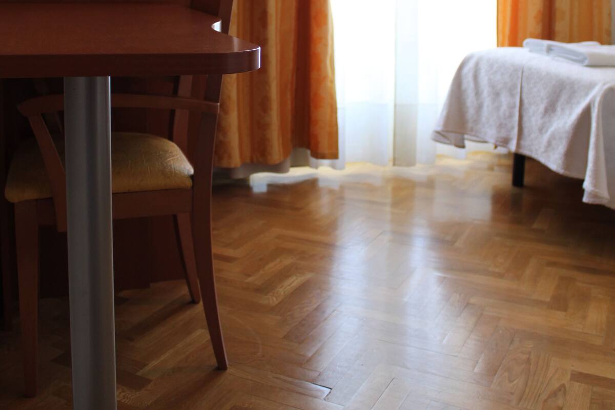 A room with a wooden floor, a dining table with chairs, and a bed with a white bedspread.