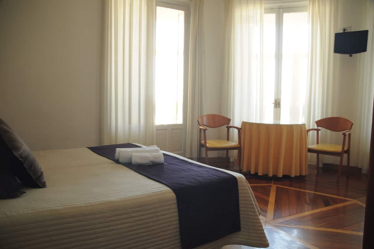 A hotel room with a bed, two chairs, a small table, and a TV.