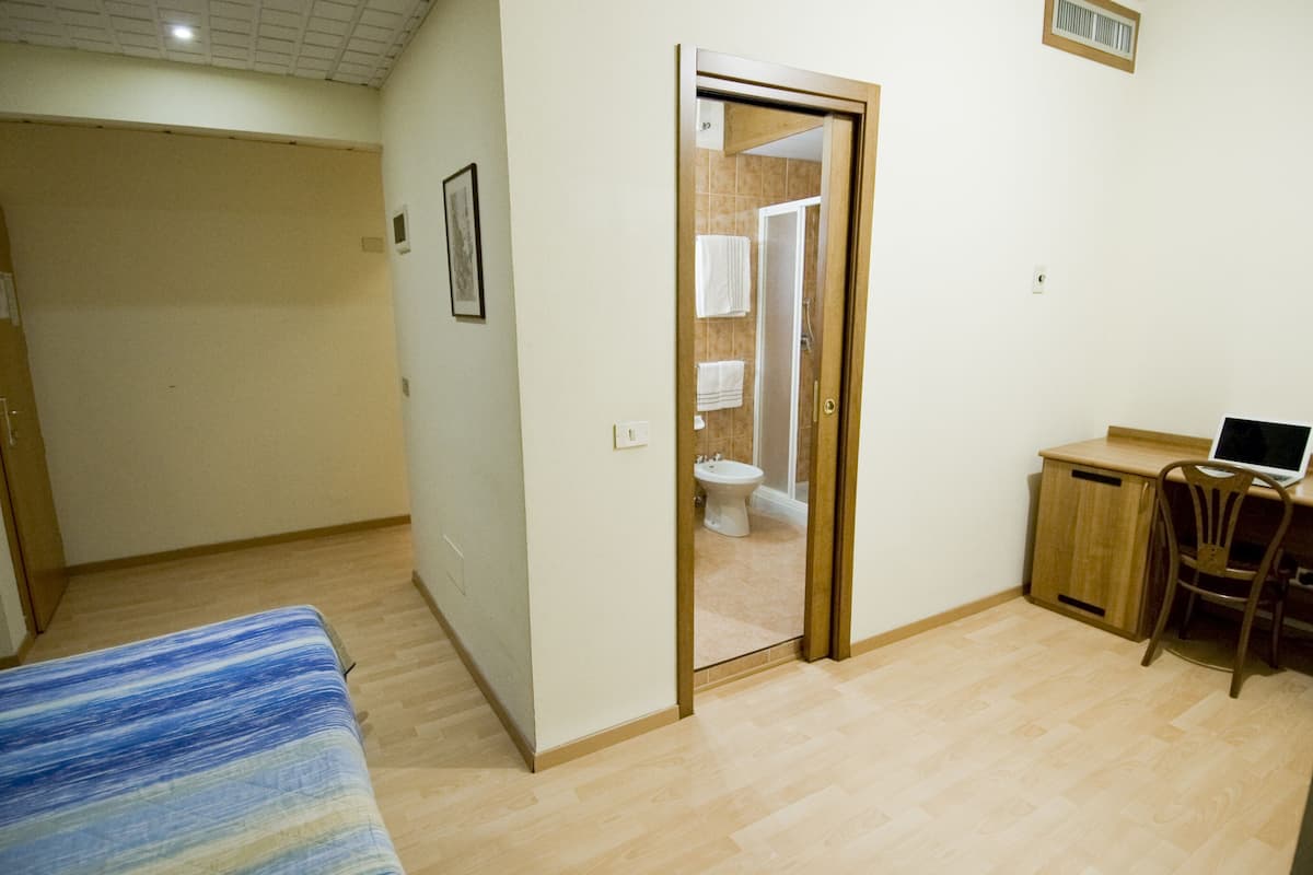 Un dormitorio con cama, escritorio y silla, y un baño visible a través de una puerta abierta.