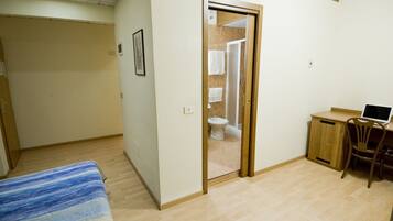 A bedroom with a bed, a desk with a chair, and a bathroom visible through an open door.