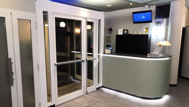 A reception area with a counter, a television, and a glass door entrance. - Europa (Sondrio)