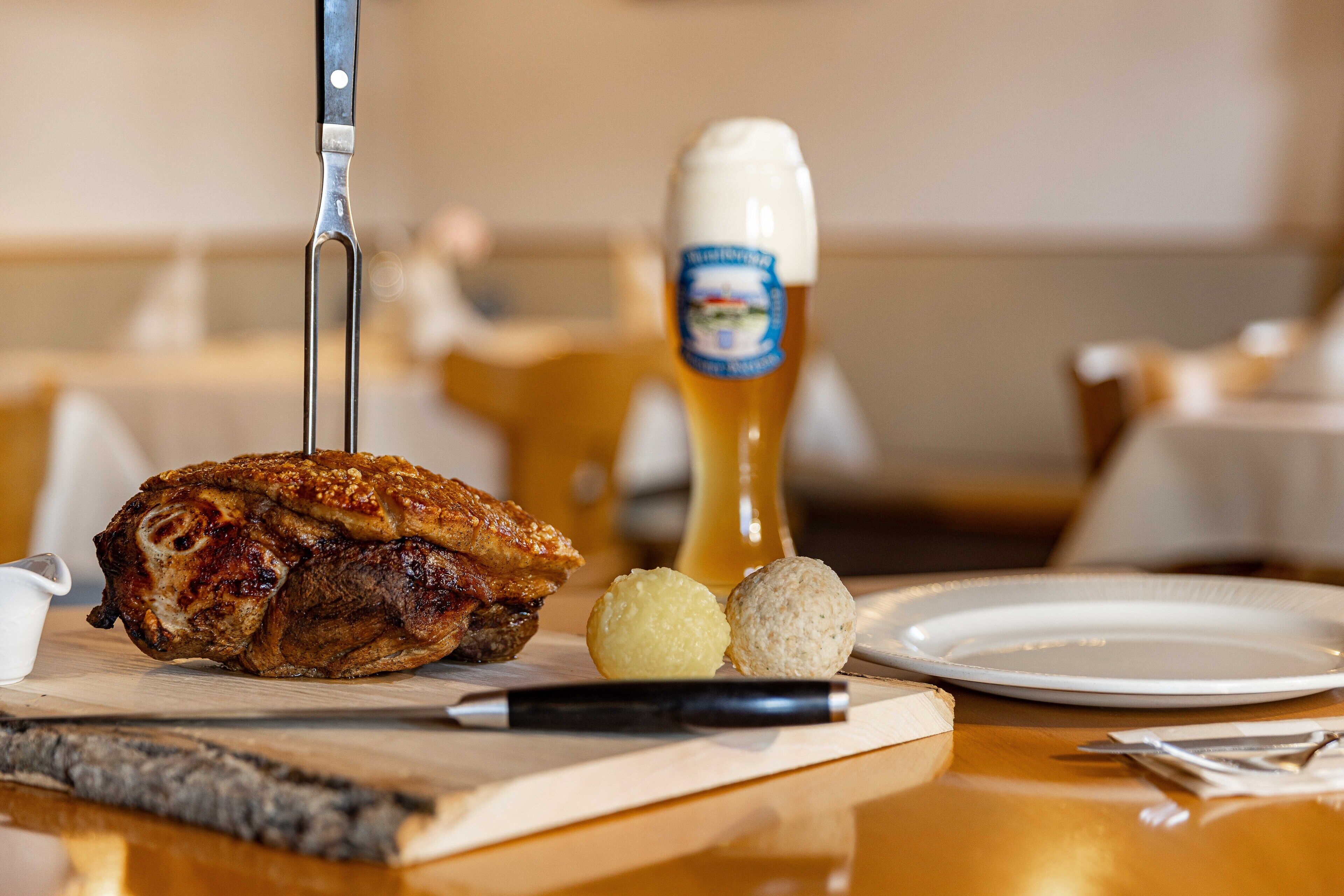 A dining table with a roasted chicken, a bottle of beer, and two bread rolls.