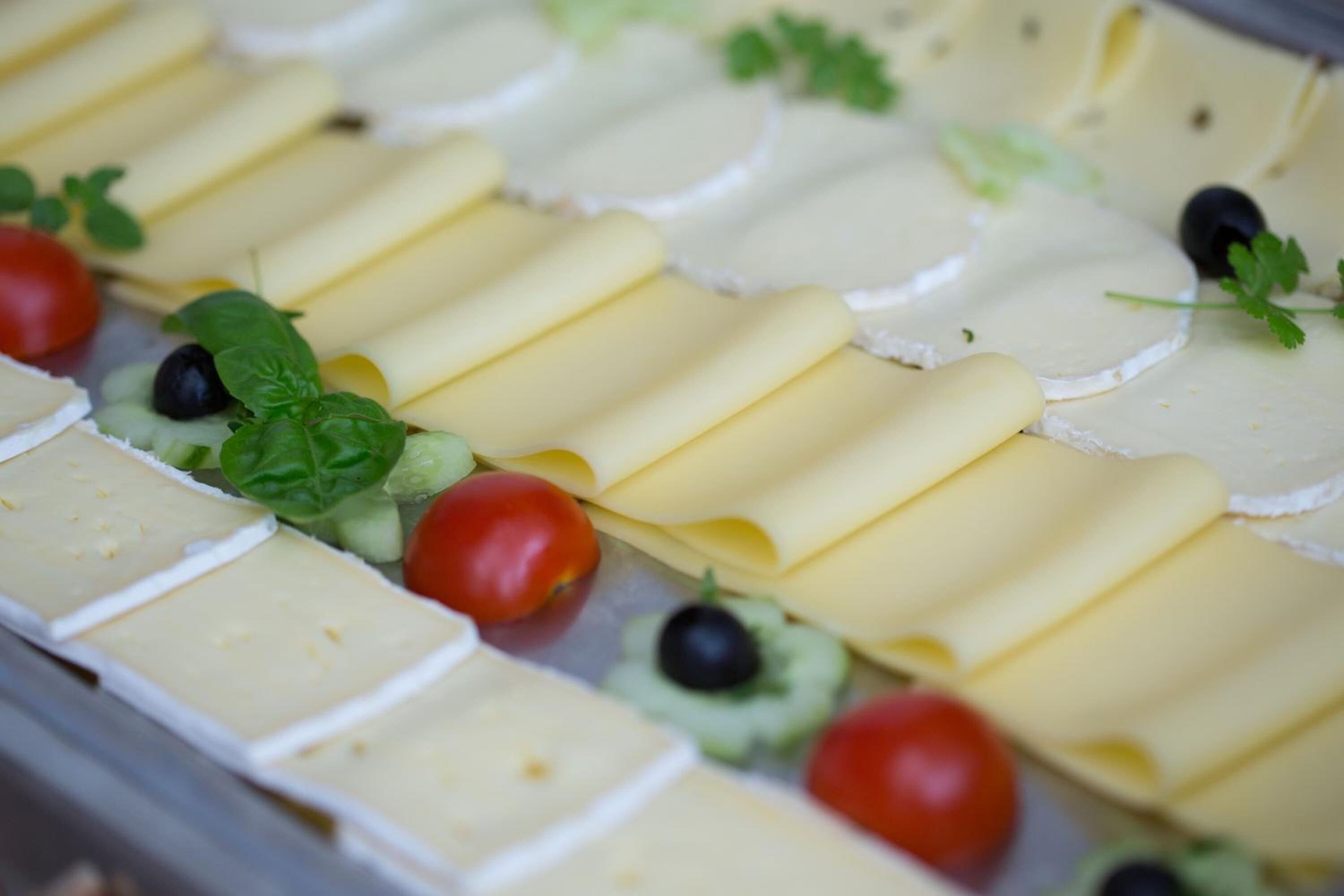 A cheese board with various types of cheese, tomatoes, olives, and herbs.
