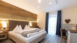 A modern hotel room with a large bed, wooden headboard, bedside lamps, a desk, and a chair. - Hotel am Wald (Bad Toelz)