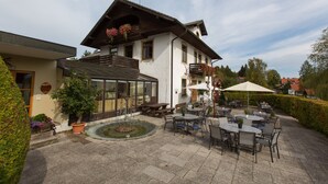 A building with a patio area featuring outdoor seating and a small garden. - Hotel am Wald (Bad Toelz)